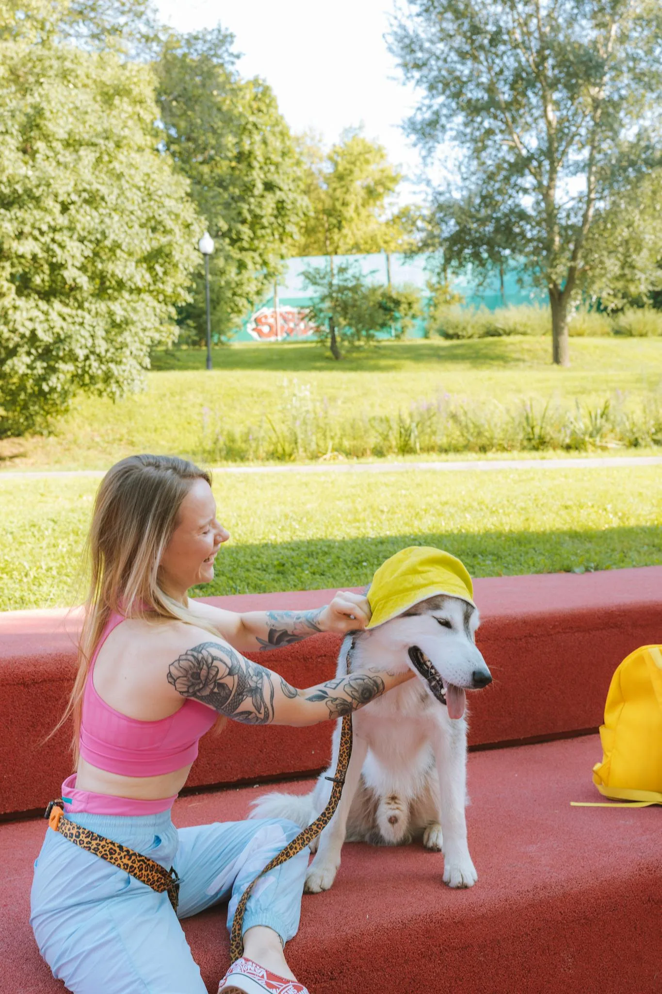 A woman in a pink tank top plays with a Siberian husky on a red bench in a sunny park.
